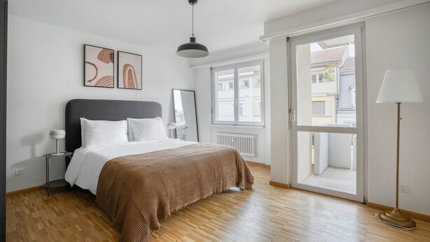 Ein Schlafzimmer mit Bett, Fenster, Tür und Lampe.