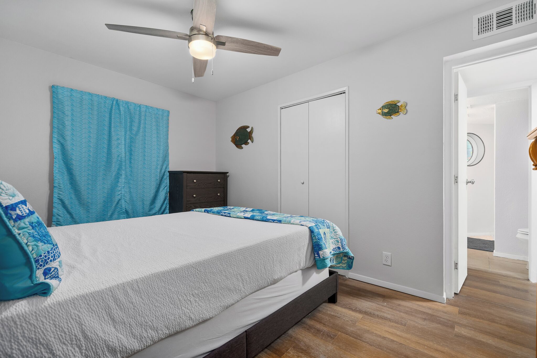 A bedroom with a bed, a ceiling fan, a wardrobe, and a door leading to another room.