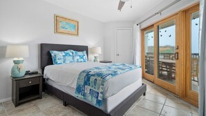 A bedroom with a bed, nightstands, a ceiling fan, a painting, and a sliding glass door to a balcony.