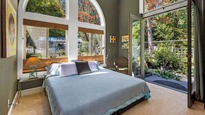 Un dormitorio con una cama grande, una ventana con vistas a árboles y una silla junto a la ventana.