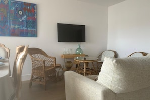 A living room with wicker furniture, a round table, a flat-screen TV, and a colorful abstract painting on the wall.