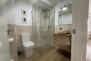 A bathroom with a glass-enclosed shower, a toilet, a sink with a marble countertop, and two framed pictures on the wall. - Desconectaengalicia Rosalía II, 100m Silgar Beach (Sanxenxo)