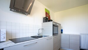 A modern kitchen with white cabinets, a stainless steel range hood, a built-in oven, and a tiled backsplash. - Holiday Home 'Maison Bretonne' with Private Terrace, Private Garden and Balcony (Ploumagoar)