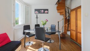 A dining area with a glass table, black chairs, a vase with flowers, a staircase, and a wooden door. - Holiday Home 'Maison Bretonne' with Private Terrace, Private Garden and Balcony (Ploumagoar)