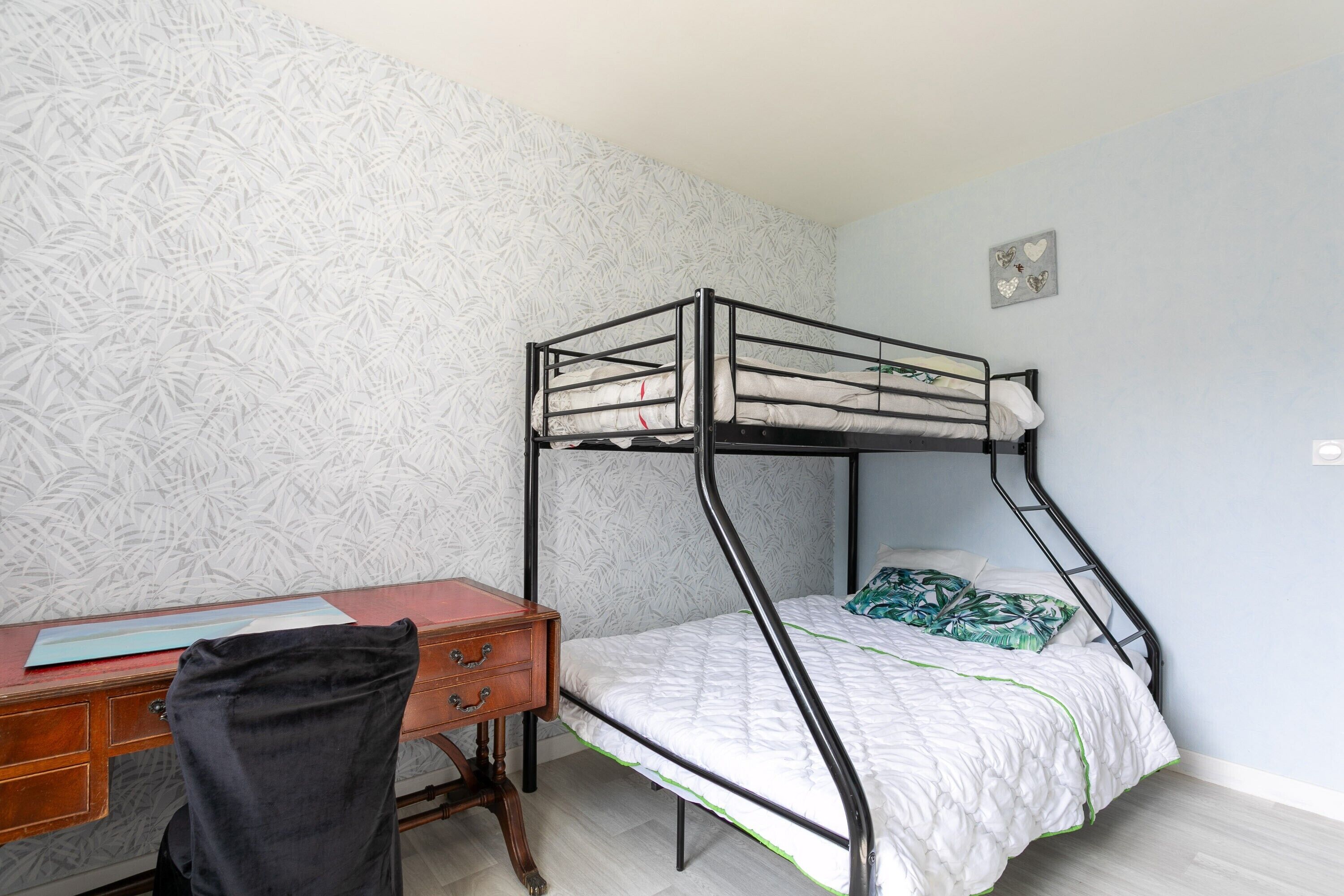 A bunk bed with a desk and chair, a patterned wallpaper, and a small decorative item on the wall.