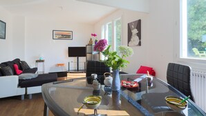 A modern living room with a glass coffee table, a sofa, a black chair, and a view of the outdoors through large windows. - Holiday Home 'Maison Bretonne' with Private Terrace, Private Garden and Balcony (Ploumagoar)