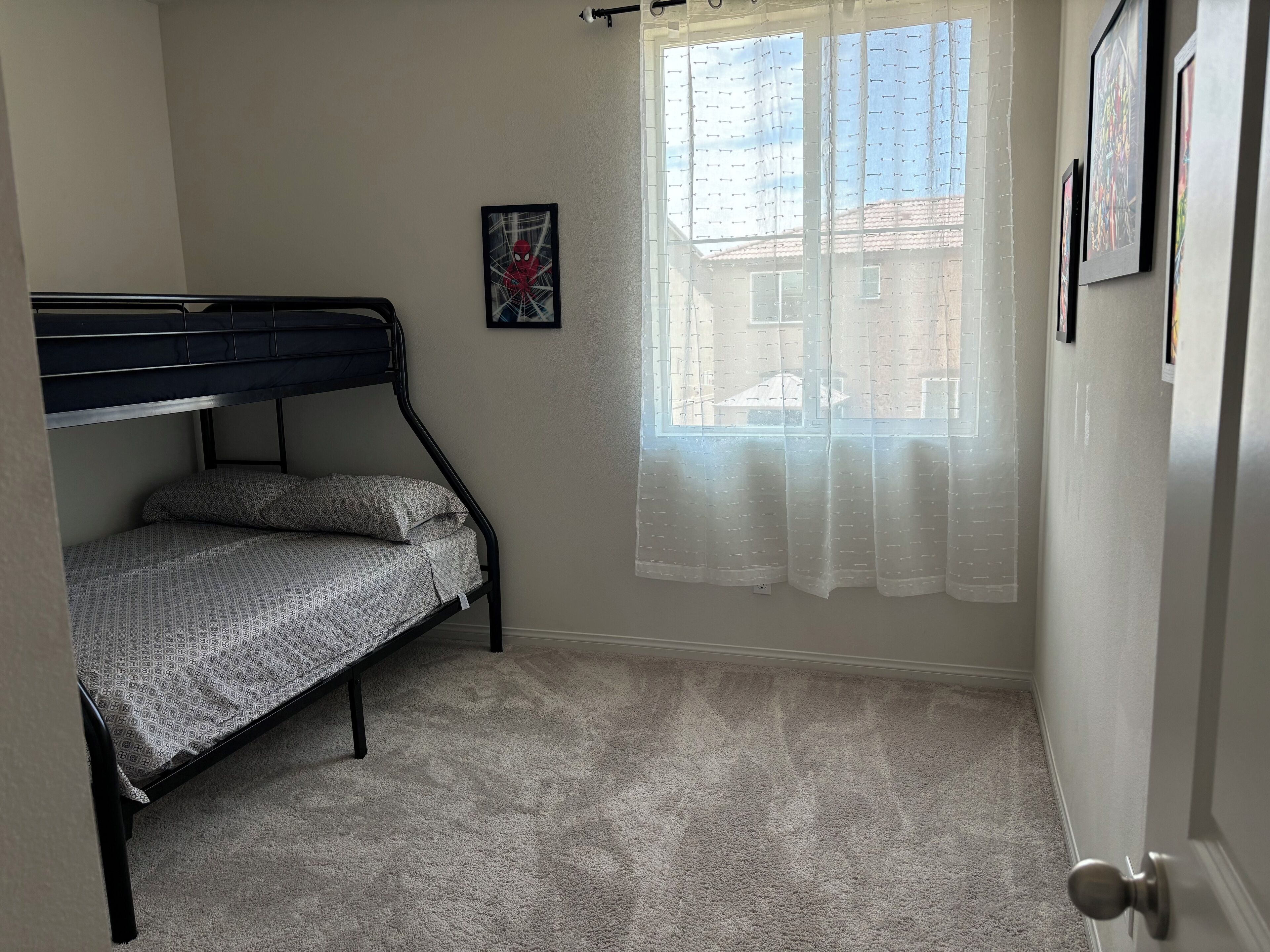 Een slaapkamer met een stapelbed, een raam met dunne gordijnen en een ingelijste foto aan de muur.
