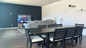 A modern dining area with a dark wooden table and chairs, a grey sofa, and a flat-screen TV displaying sports content. - BEAUTIFUL 2 STORY HOUSE IN MORENO VALLEY (Moreno Valley)
