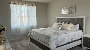A bedroom with a bed, nightstands, a window with curtains, a wall art piece, and a vase with flowers. - BEAUTIFUL 2 STORY HOUSE IN MORENO VALLEY (Moreno Valley)