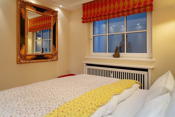 Une chambre à coucher avec un lit, une fenêtre donnant sur un beau paysage, un radiateur et un miroir doté d’un cadre décoratif.