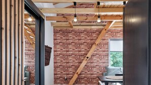 A modern interior with exposed wooden beams, a brick wall, and a dining area with a table and chairs. - Starołęcka Apartment with Mezzanine (Poznań)