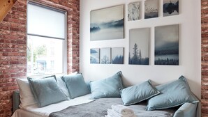 A bedroom with a loft-style ceiling, exposed brick walls, a large bed with multiple pillows, and a series of landscape paintings on the wall. - Starołęcka Apartment with Mezzanine (Poznań)