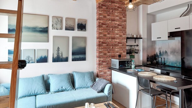 A modern living space with a wooden ceiling, a brick wall, and a kitchen area. - Starołęcka Apartment with Mezzanine (Poznań)