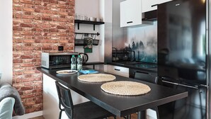 A modern kitchen with a brick wall, stainless steel appliances, and a dining area with stools. - Starołęcka Apartment with Mezzanine (Poznań)