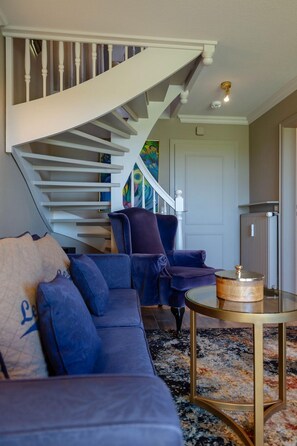 Uma sala de estar moderna com um sofá em forma de L azul, uma mesa de centro de vidro e uma escada com guarda-corrimão branco.