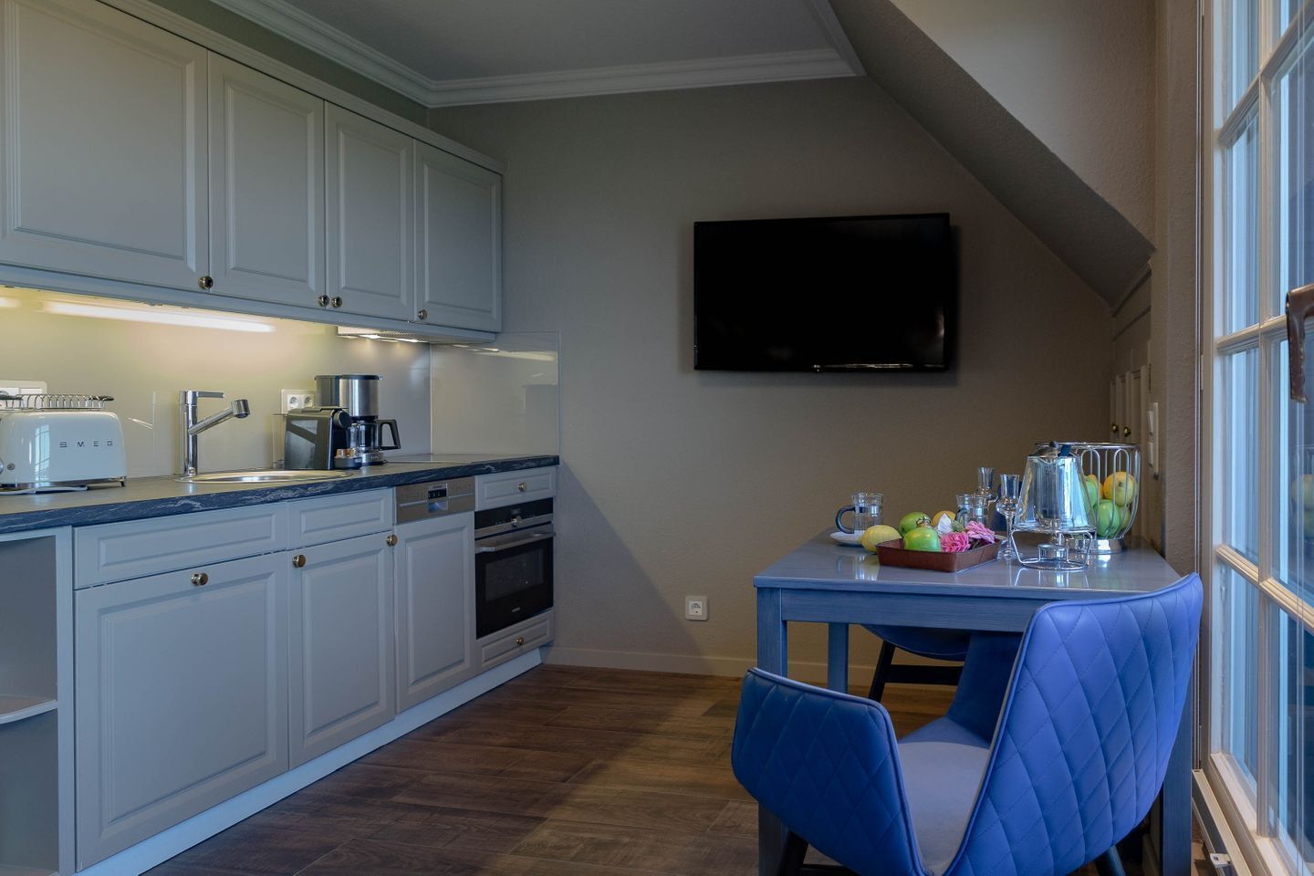 A kitchen with white cabinets, a coffee maker, a toaster, and a table with fruit and glasses.