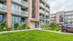 Un edificio residencial de varios pisos con balcones, entrada para vehículos y un coche estacionado.