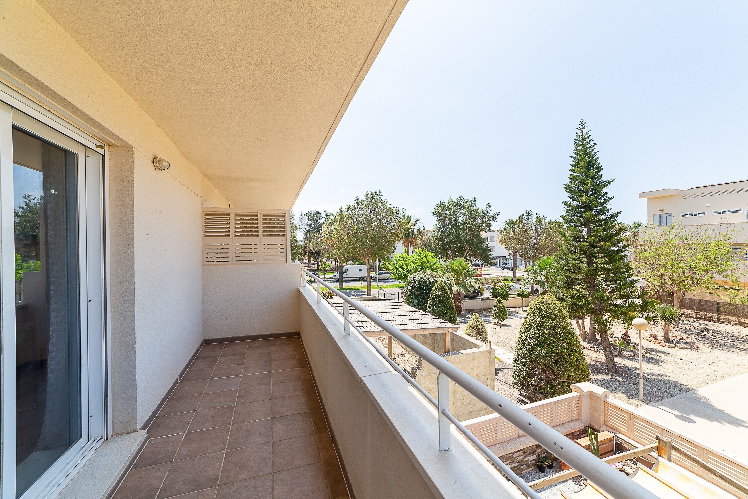Un balcón con vista a un área ajardinada, que incluye árboles y un edificio al fondo.