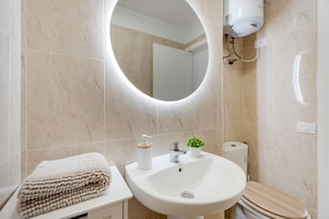 Une salle de bain équipée d’un lavabo, de toilettes et d’un miroir avec un éclairage intégré.