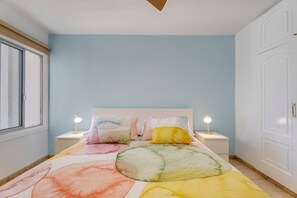 Une chambre à coucher avec un lit, deux tables de chevet avec des lampes, une fenêtre et une porte.