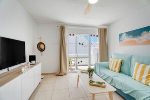 Un salon moderne doté d’un téléviseur à écran plat, d’un canapé avec des coussins à rayures, d’une table basse et d’une vue sur l’extérieur, visible à travers une porte vitrée.