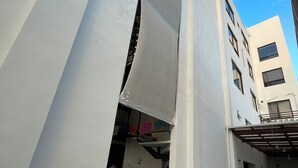 A narrow alleyway with a white building on one side and a multi-story building on the other. There is a door with a curtain partially drawn, and a small orange pumpkin decoration on the floor. - Torre Yaxche 39 (Cancun)
