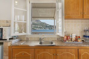 A kitchen with a view of a coastal town, a sink, and various food items on the counter.