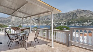 Un espace extérieur aménagé, abrité et doté de tables et de chaises, offrant une vue sur un paysage montagneux et une étendue d’eau.