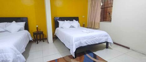 A hotel room with two beds, a small table, and a window with curtains.