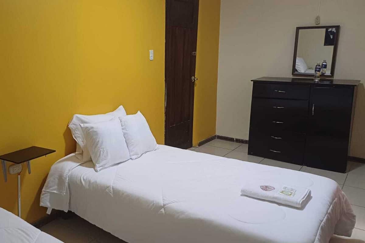 A hotel room with two beds, a small bedside table, a dresser, and a mirror.