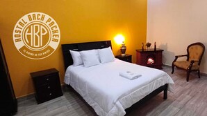 A hotel room with a bed, a nightstand, a chair, and a fireplace. - Back Packer (Ibarra)