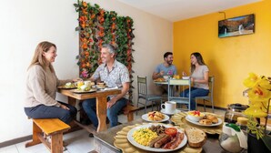 A dining area with a wooden bench, a table with breakfast items, and a decorative wall with foliage. - Back Packer (Ibarra)