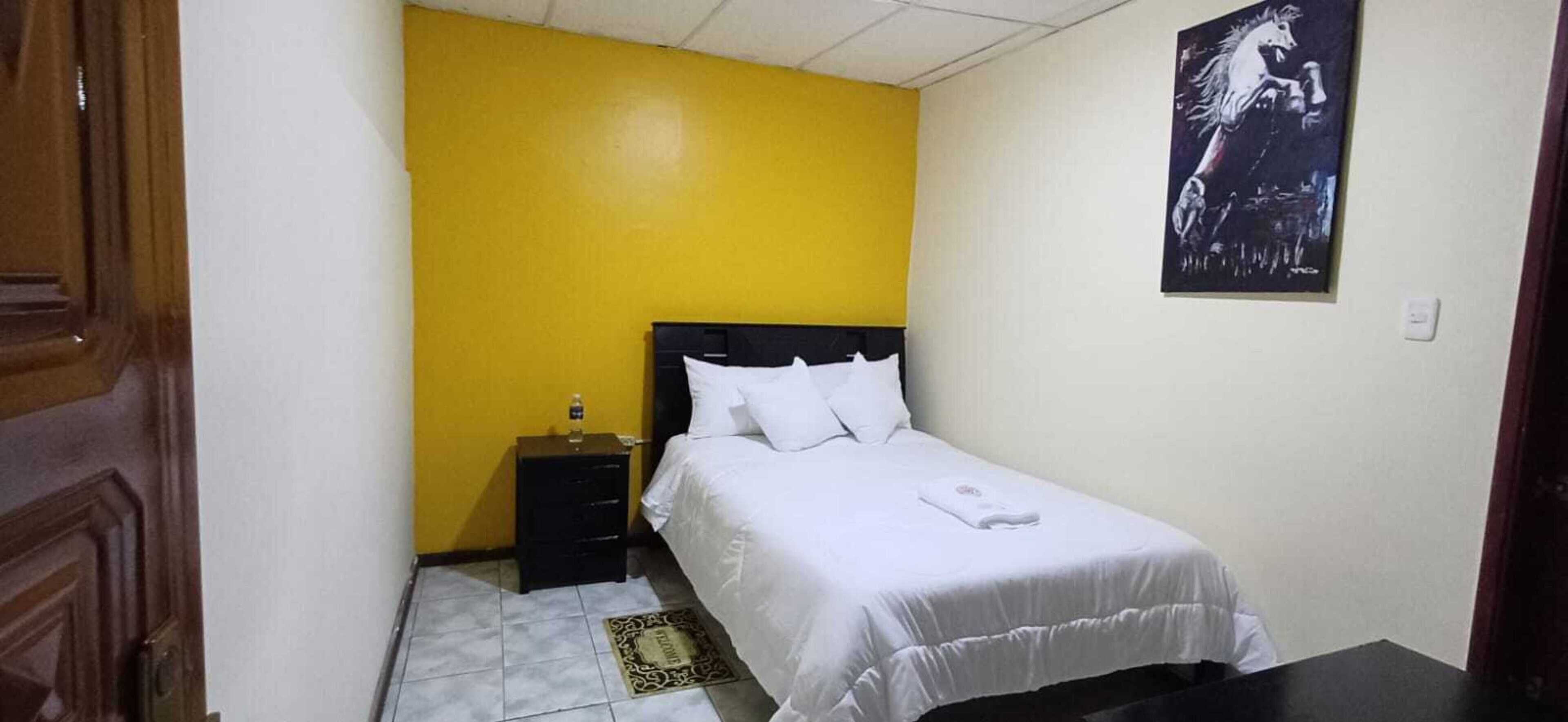 Un dormitorio pequeño y ordenado con una cama individual, una mesita de noche y un cartel en la pared.