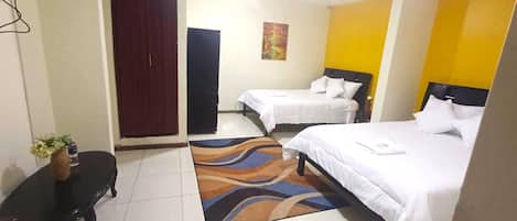 A hotel room with two beds, a small table with a vase, and a colorful rug.