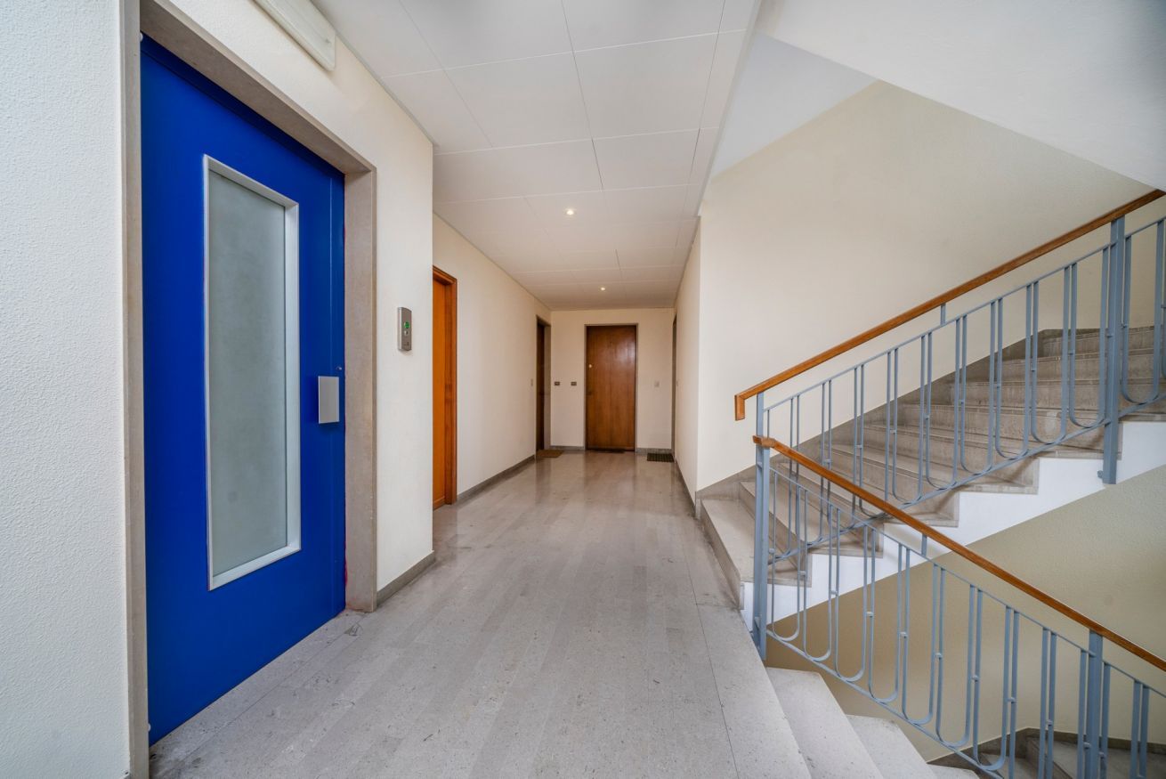 A hallway with a blue door, a staircase with metal railings, and a light-colored floor.