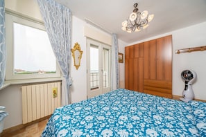 Une chambre à coucher comprenant un lit, un radiateur, une fenêtre avec des rideaux, une armoire en bois et un ventilateur de plafond.