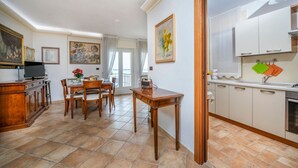 A dining area with a table and chairs, a kitchen with cabinets and a sink, and a painting on the wall. - GuestHost - Relais Rosanna Stunning Lagoon-View Apartment (Grado)