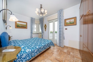 A bedroom with a bed, a table, a chandelier, and a view through the door.