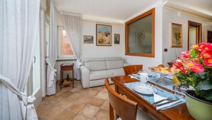 A dining area with a table set for breakfast, a sofa, and a window with curtains. - GuestHost - Relais Rosanna Stunning Lagoon-View Apartment (Grado)