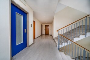 A hallway with a blue door, a staircase with metal railings, and a light-colored floor.
