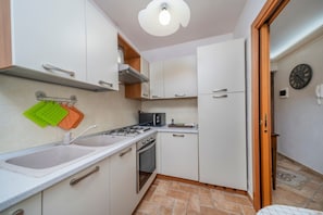 Une cuisine de taille réduite, avec des meubles blancs, une cuisinière à gaz, un évier et un four à micro-ondes.