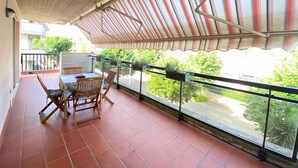 Un balcon doté d’un sol carrelé, d’une table avec des chaises et d’une balustrade agrémentée de plantes en pot.