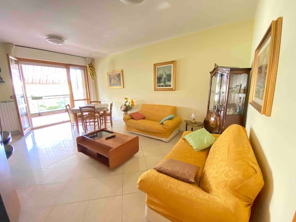 A living room with a sofa, a coffee table, a dining table with chairs, and a balcony with a view.
