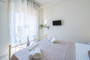 A hotel room with a bed, a TV, a mirror, and a window with curtains.