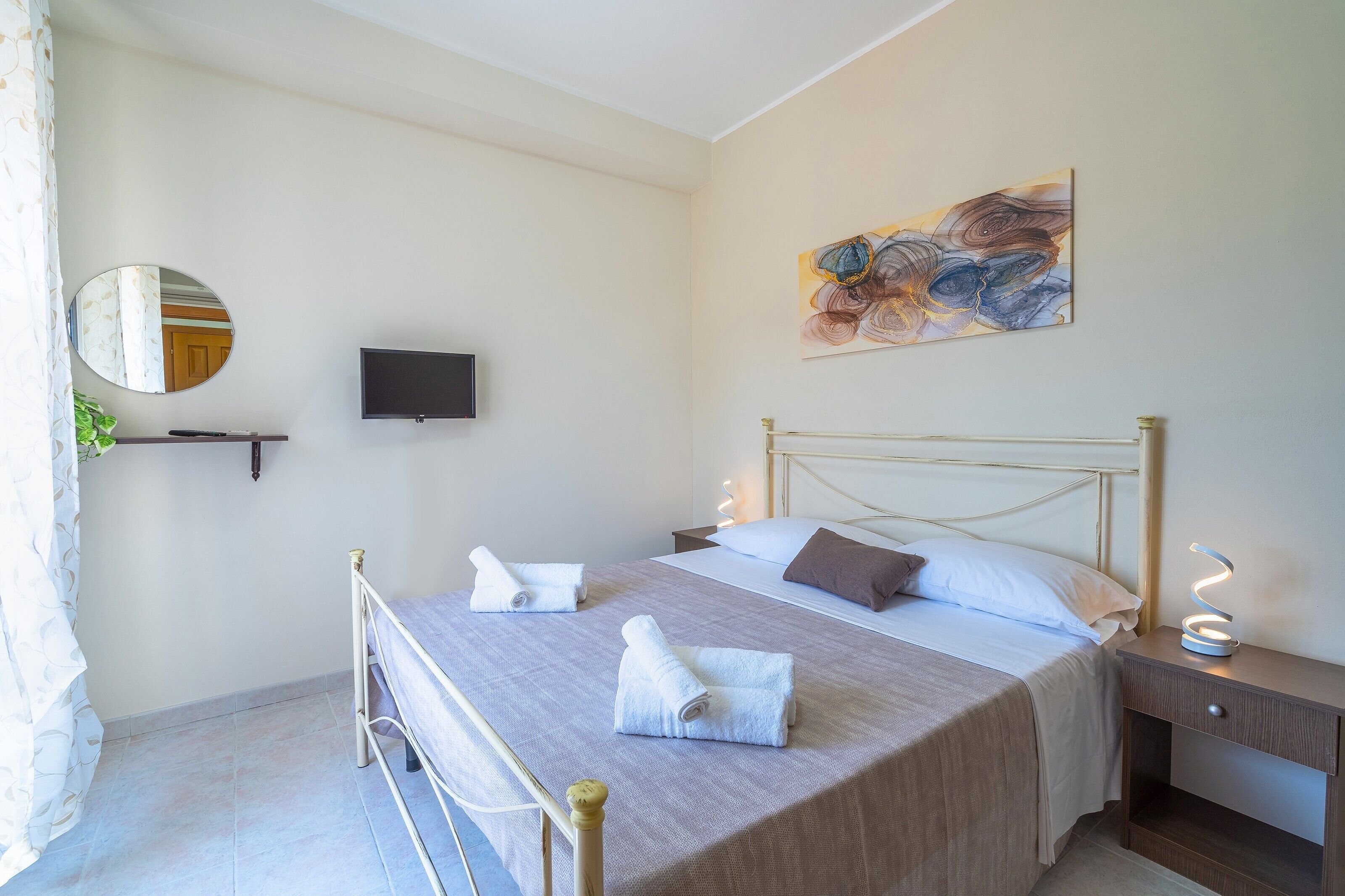 Quarto com cama, mesa de cabeceira, luminária, obra de arte e televisão.