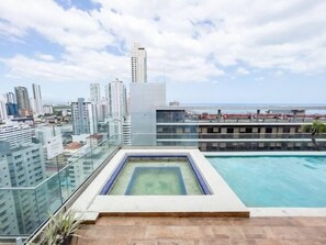 Una piscina en la azotea con barandilla de cristal, con vistas a un paisaje urbano de edificios altos y cielo despejado.