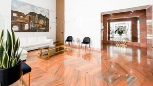 A modern lobby with a white sofa, two black chairs, a wooden coffee table, and a large painting of a historical building.