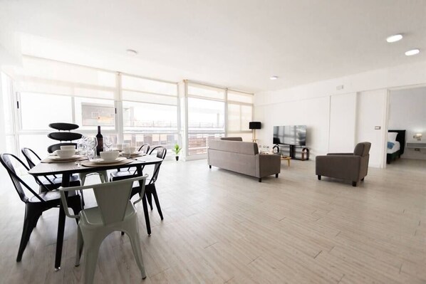Una sala de estar moderna con comedor, ventanas amplias y un televisor de pantalla plana.
