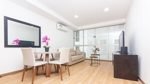 Una sala de estar moderna con comedor, un sofá, una mesa de centro, un televisor y un ventanal grande.