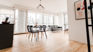 A modern living room with a dining area, large windows, and a city view.